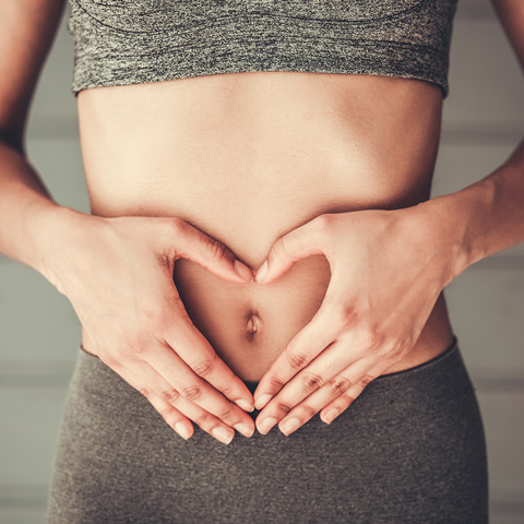 Frau formt Herz vor Bauch