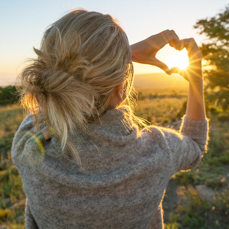 Woman forming a heart with her hands and sunshine