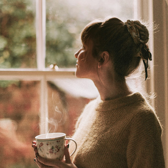 Frau mit Tasse Kaffee schaut aus dem Fenster