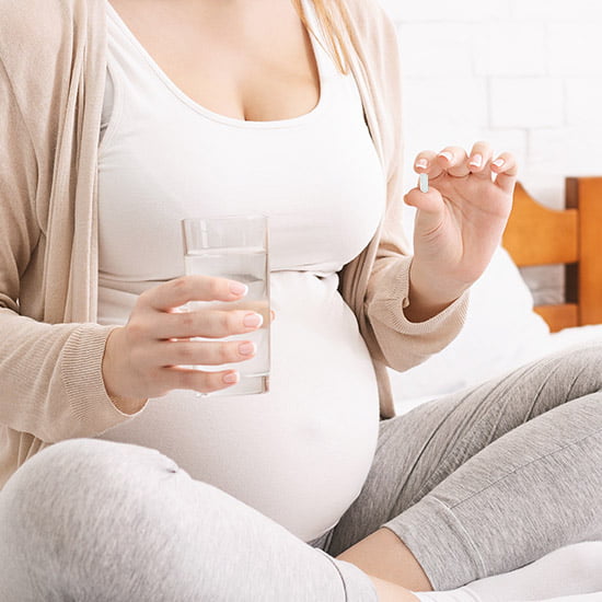 Schwangere Frau hält ein Glas Wasser und eine Jod Kapsel
