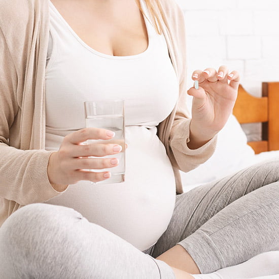 Jodpräparate in der Schwangerschaft Schwangere Frau hält ein Glas Wasser und eine Jod Kapsel