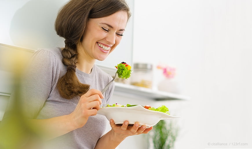 Frau sitzt in der Küche und isst Salat