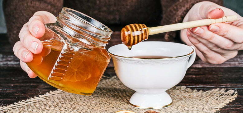 Honig wird in eine Tasse Tee geträufelt