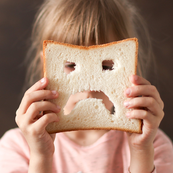 Kind hält eine Scheibe Brot mit ausgeschnittenem Gesicht vor sich.