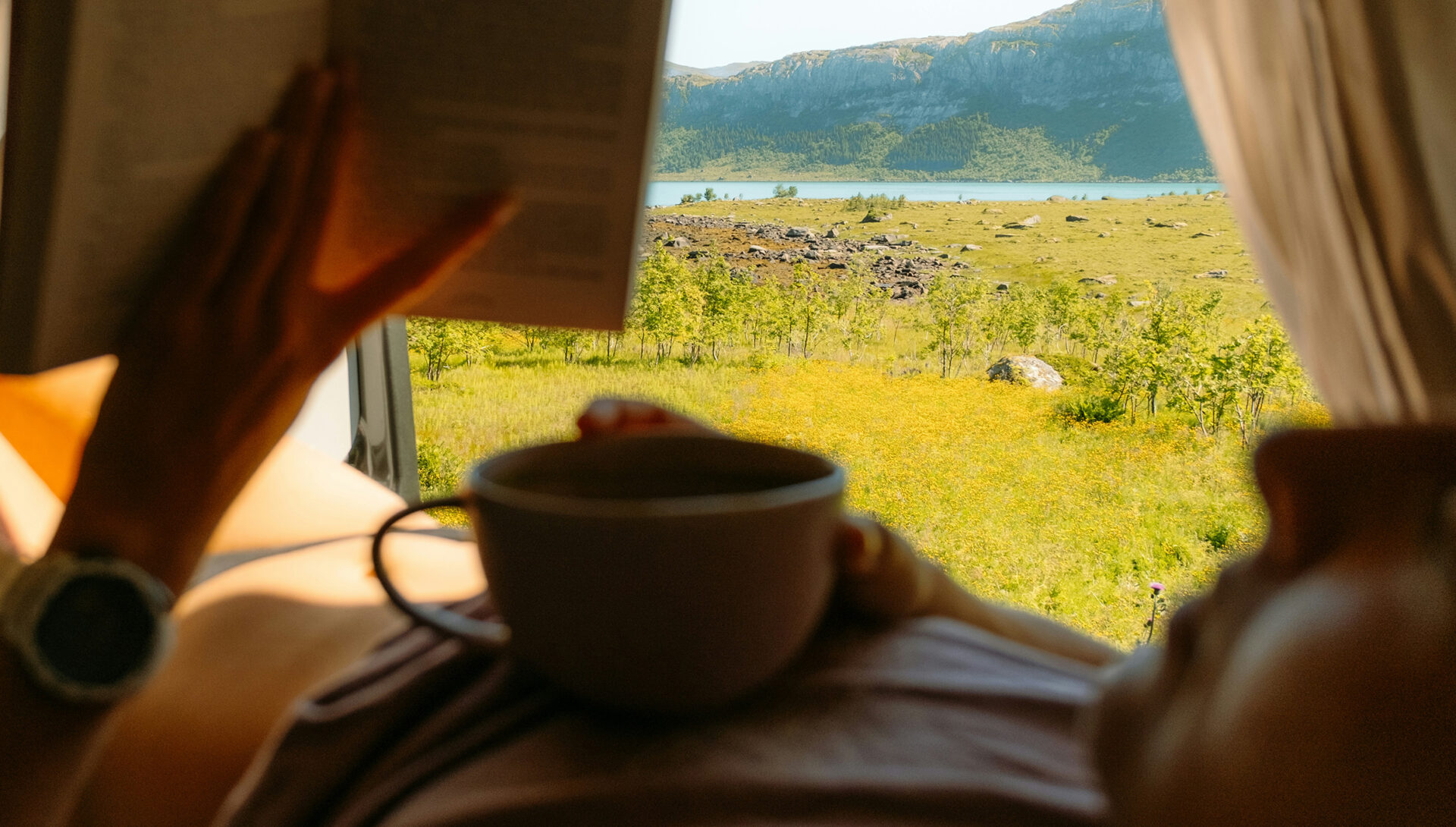 Person liest entspannt mit einer Tasse vor einer Berglandschaft
